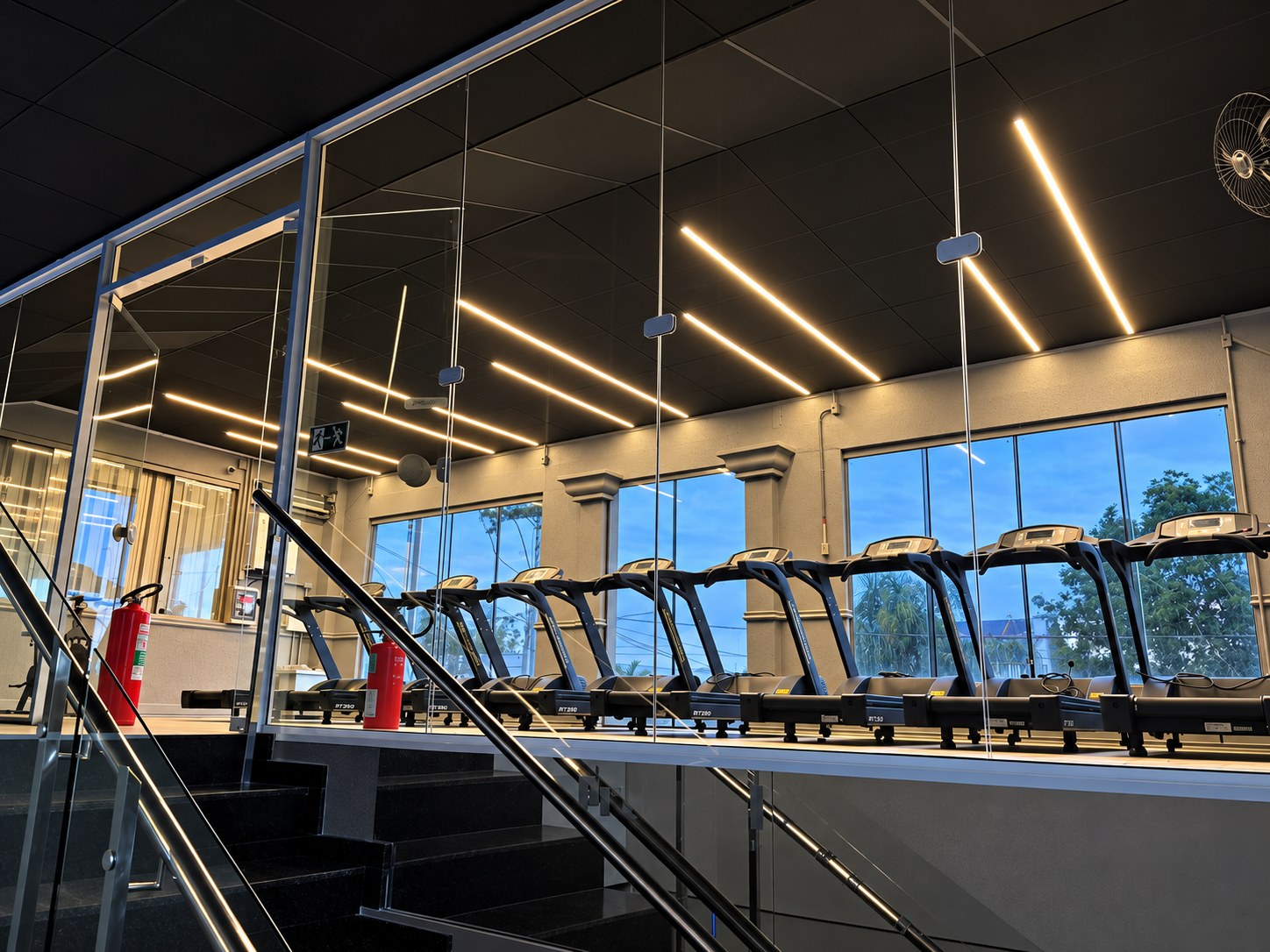 Mezanino com guarda-corpo de vidro e área de cardio ao fundo